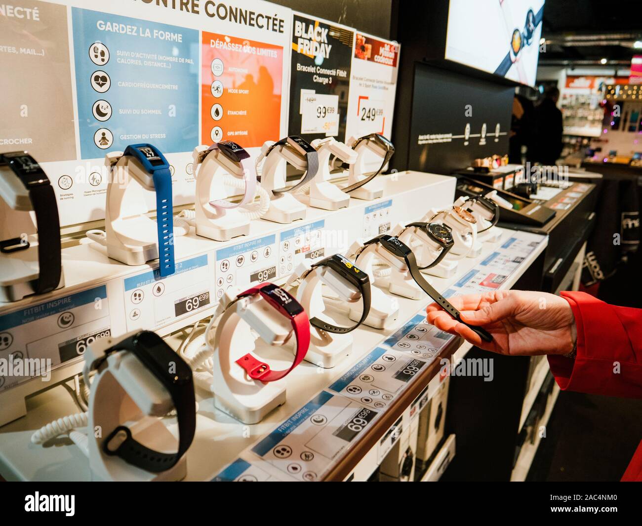 Nice, France - Nov 24, 2019: Woman in red coat looking inside electronics Fnac store at multiple types of smart watch from Fitbit before the annual Black Friday deals and offers Stock Photo