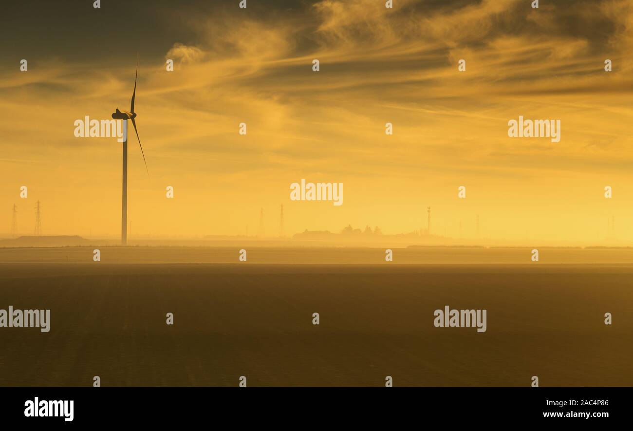 Single wind turbine captured at sunrise in the countryside of France with silhouettte of power poles at the base. Stock Photo