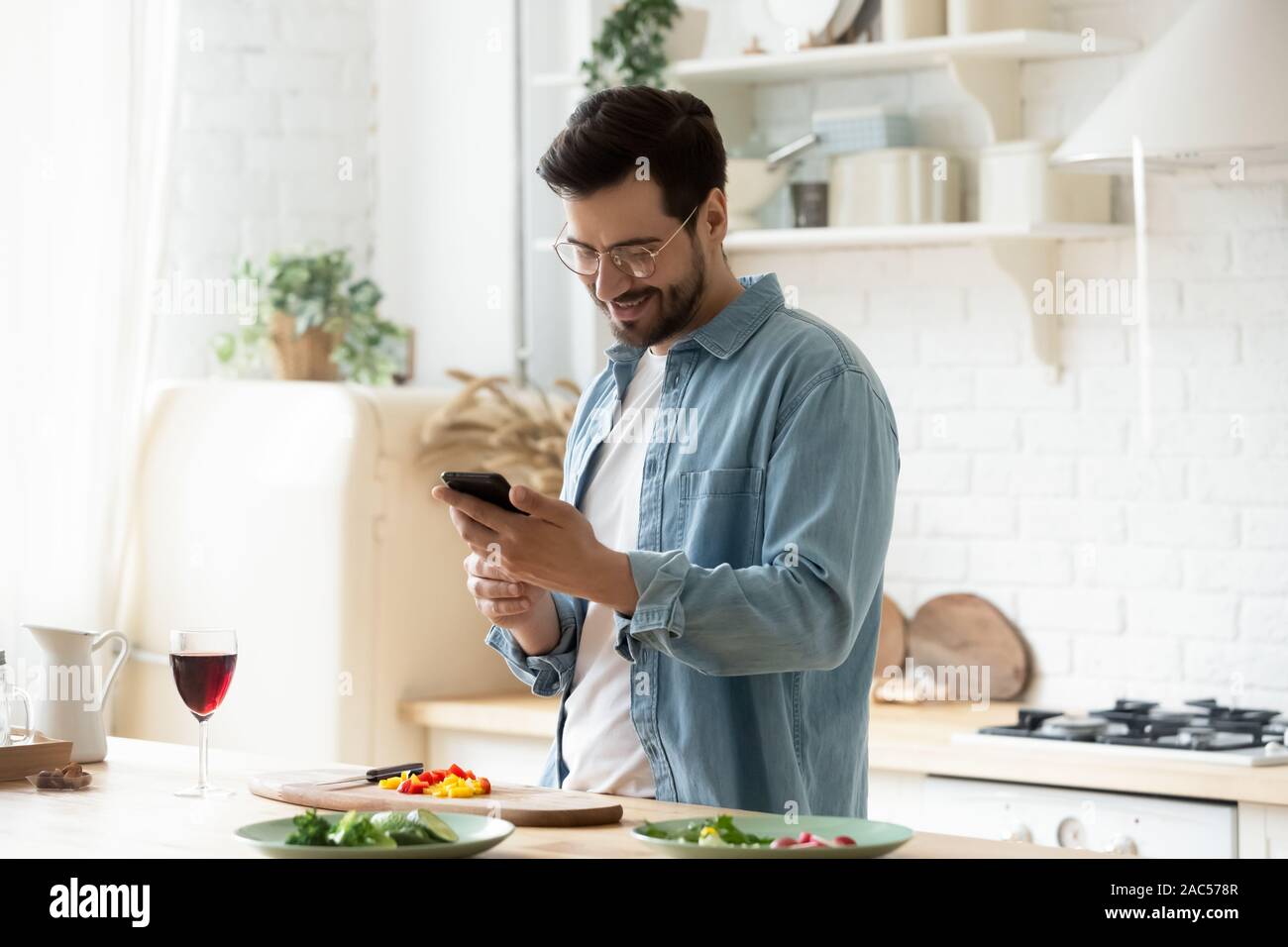 Happy young man preparing romantic dinner using smartphone app Stock Photo