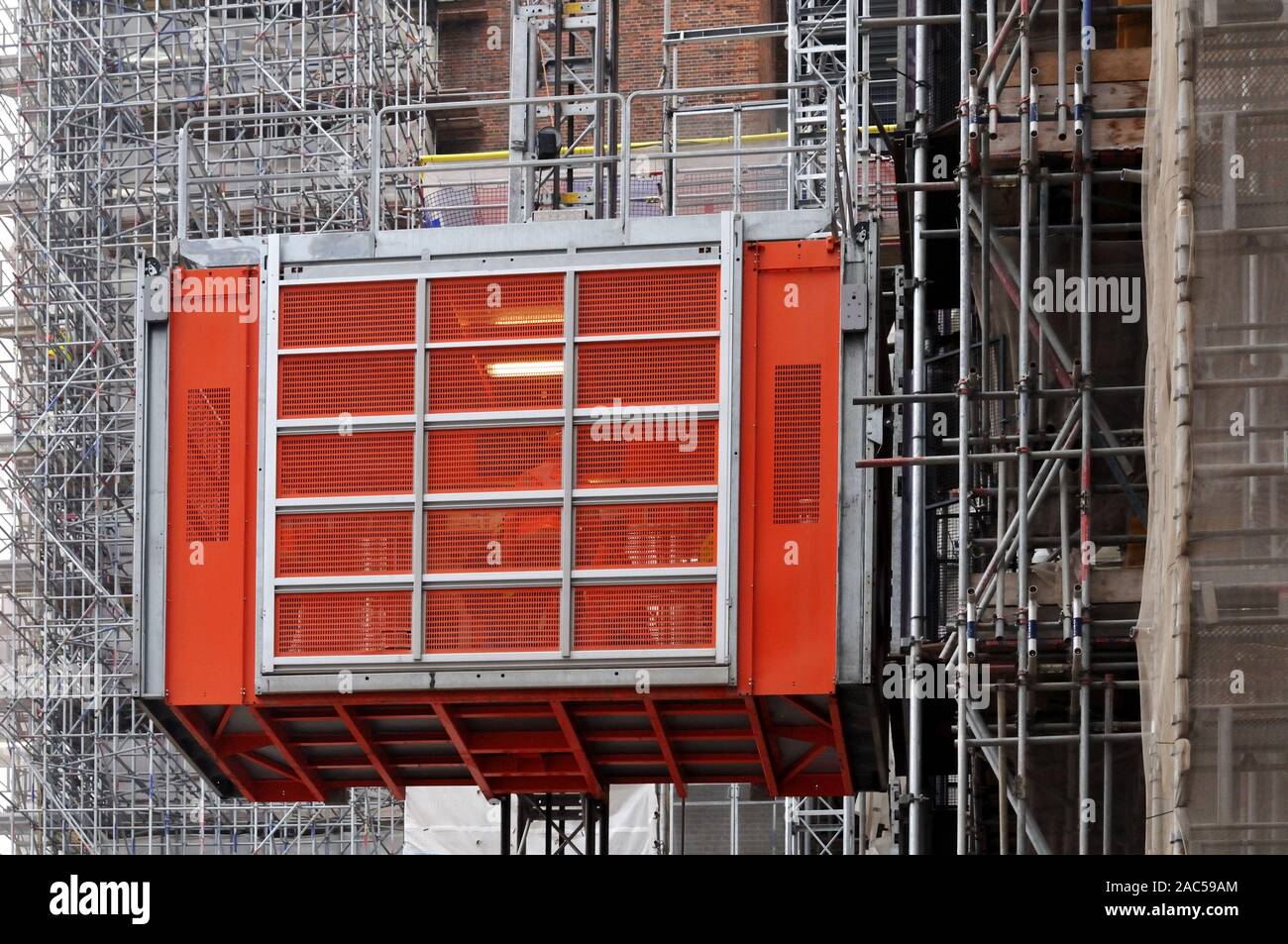 red metal elevator leading high up alongside scaffolding at facade of a