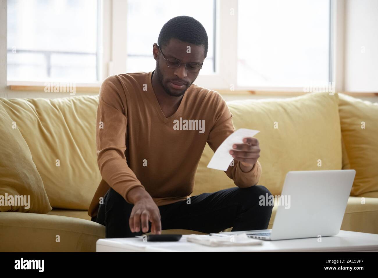 Concentrated biracial man calculating household expenses at home Stock Photo