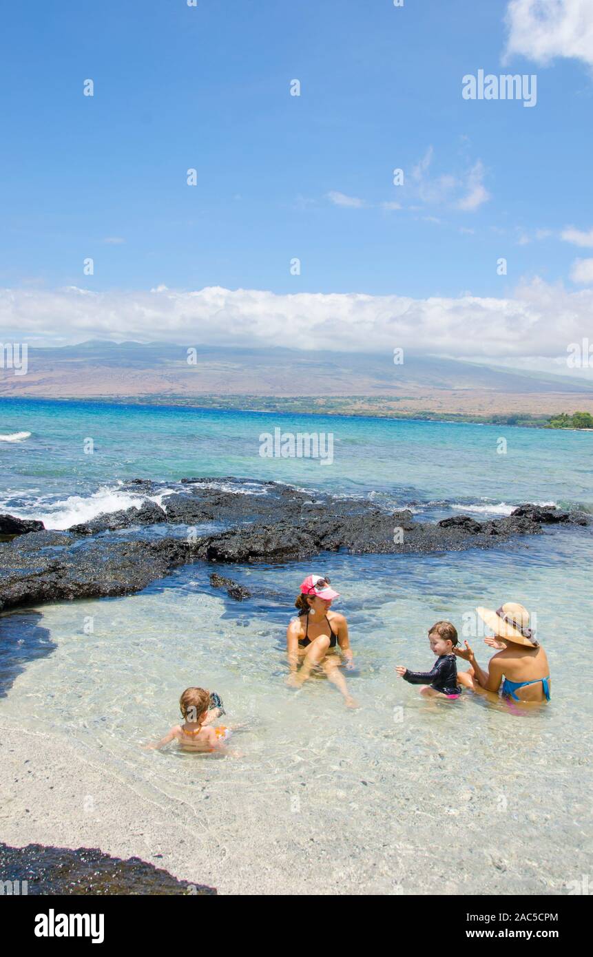 Two local moms talk and their children play in a warm tide pool at a beach in Puako, Big Island. Stock Photo