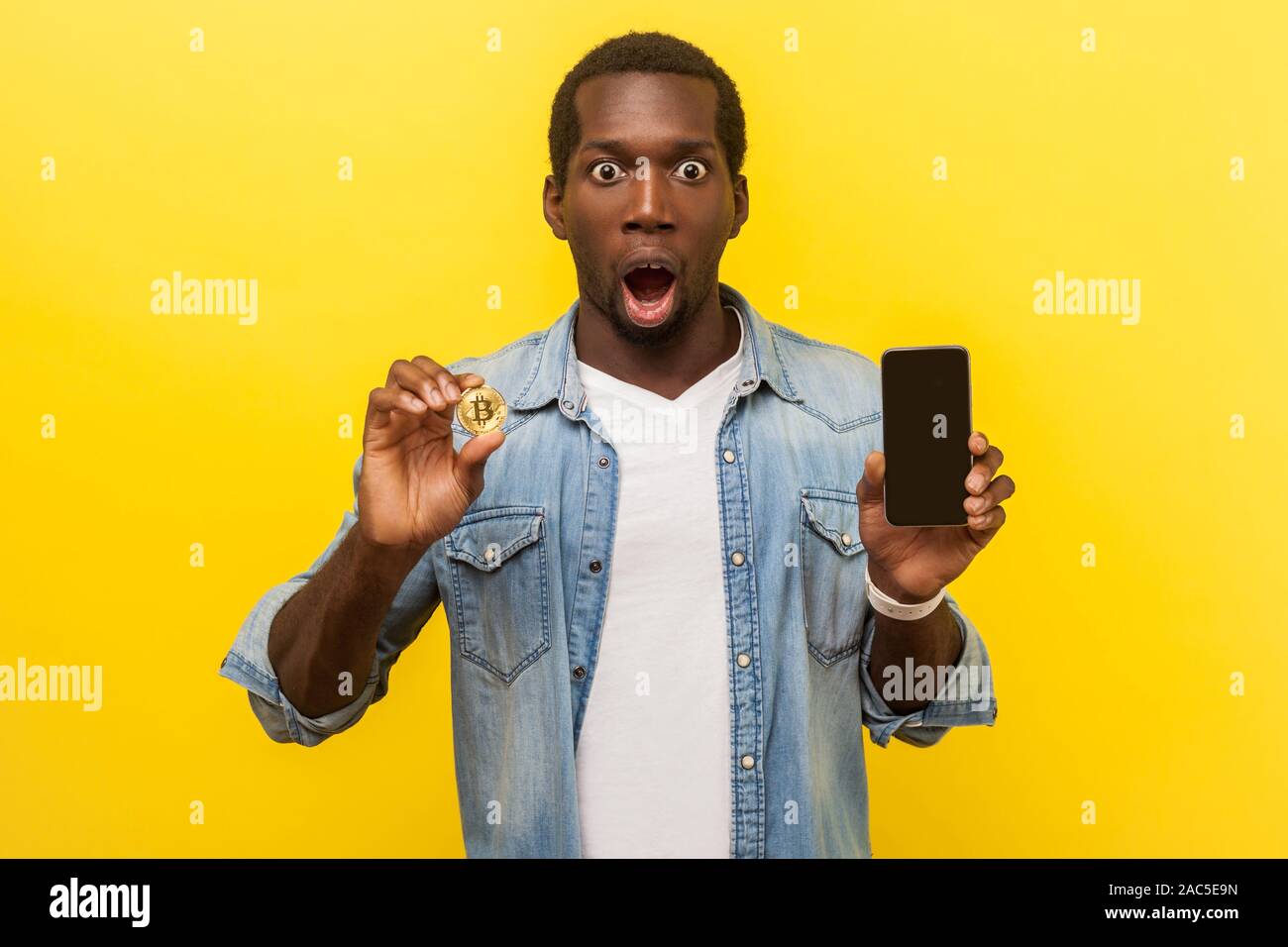 Cryptocurrency mobile app. Portrait of excited man with astonished shocked  face expression wearing casual shirt, holding cellphone and golden bitcoin  Stock Photo - Alamy