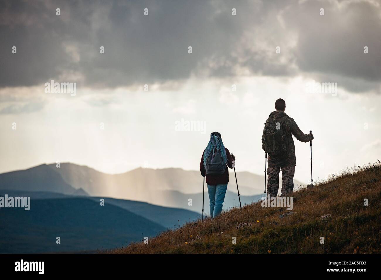 Couple of unrecognised hikers silhouettes stands with trekking poles in mountains Stock Photo