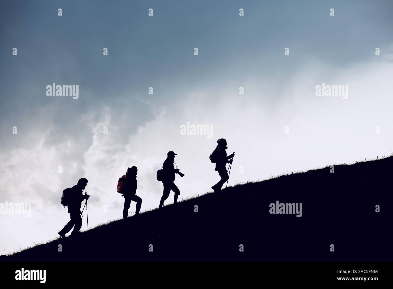 Group of four hikers silhouettes are going uphill in mountains against cloudy sky Stock Photo