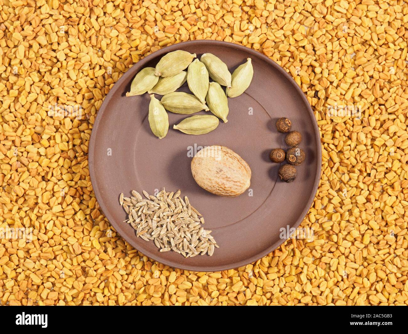 Spices in clay plate green cardamom, fennel, allspice, nutmeg. Background from Fenugreek