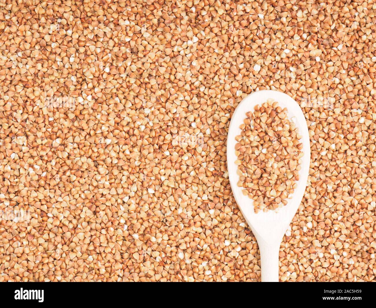 Buckwheat groats in wooden spoon on a buckwheat background. Healthy eating concept Stock Photo