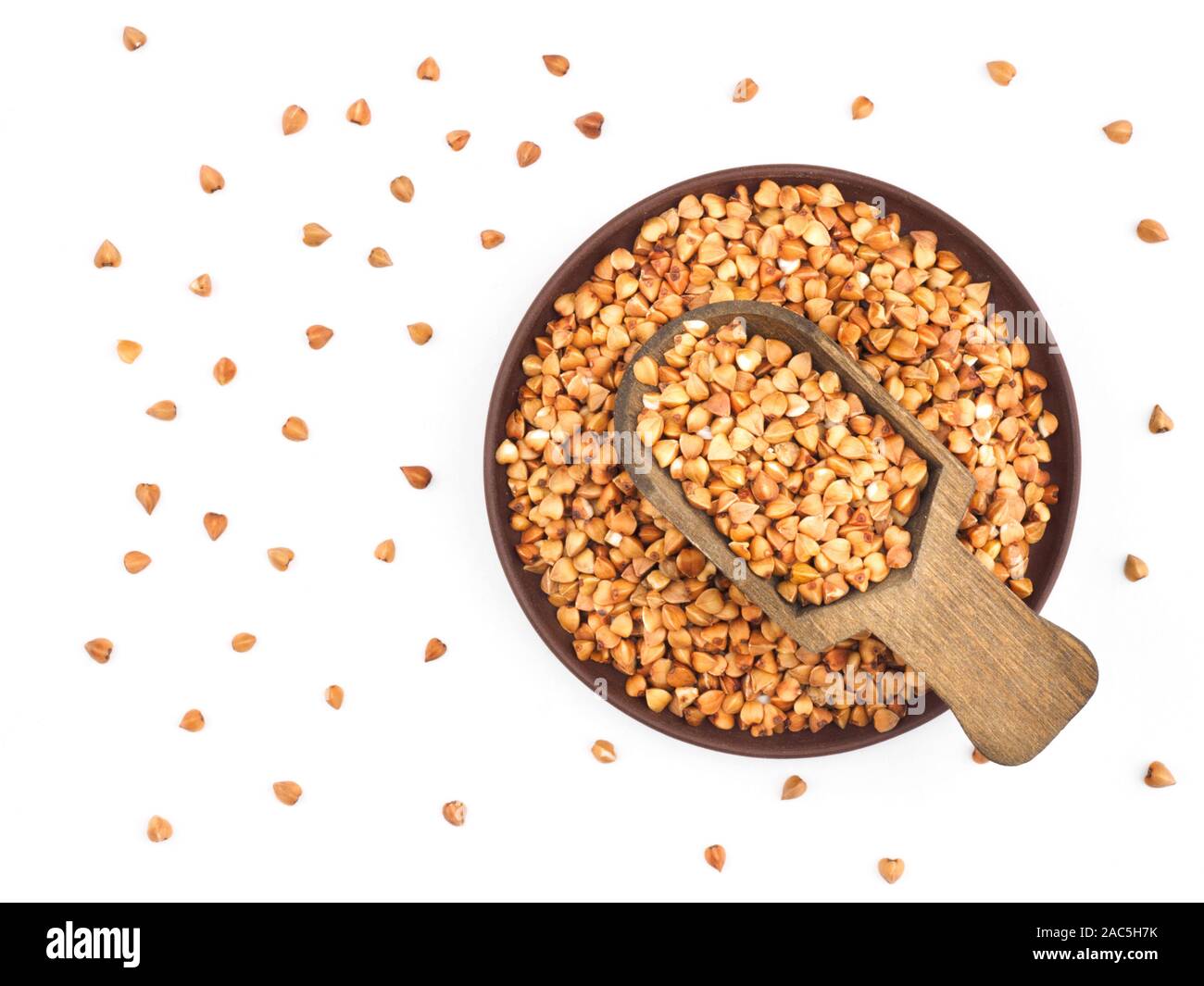 Buckwheat groats in clay plate and in wooden shovel on white background. Healthy eating concept