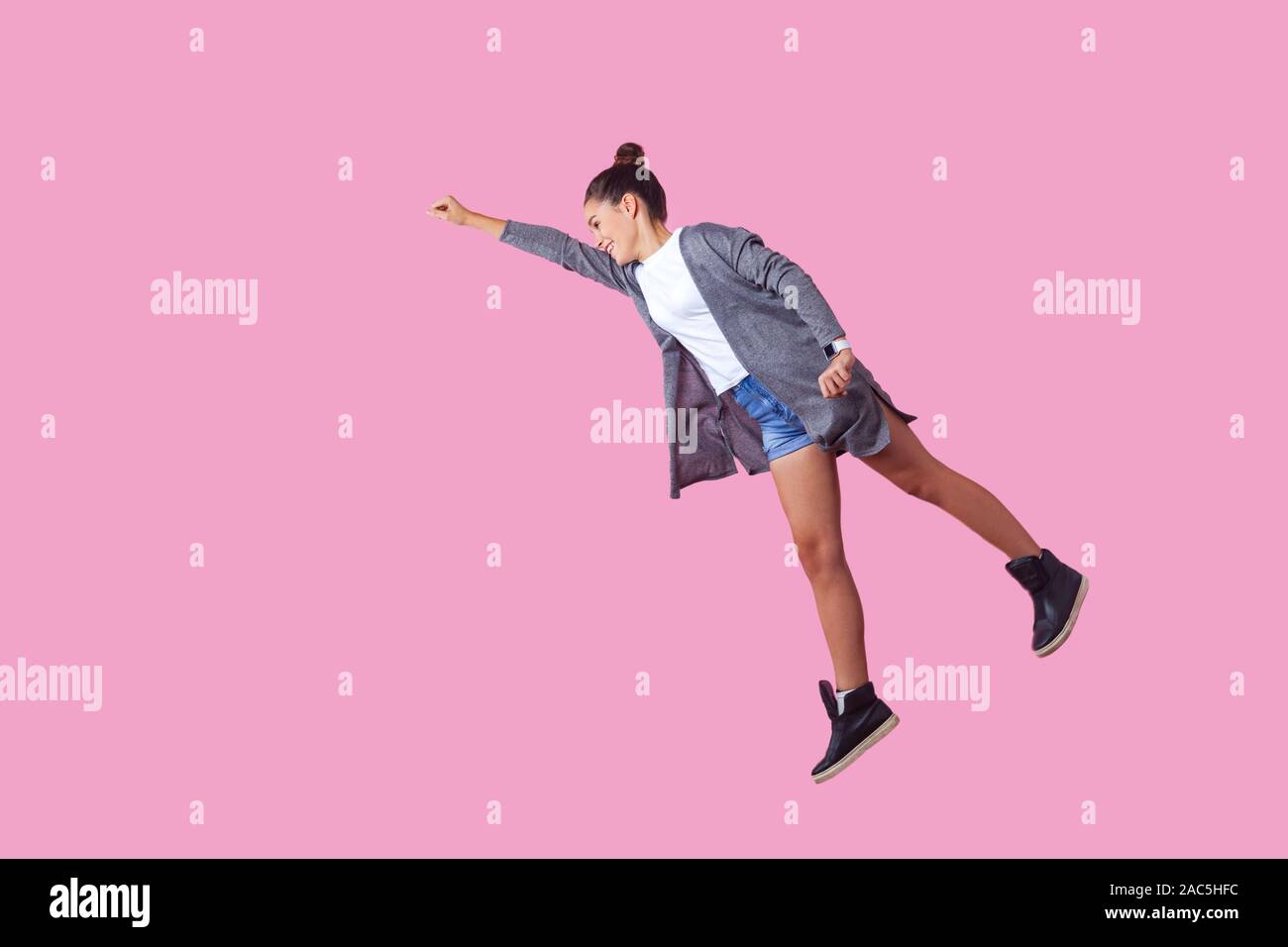 Superman. Portrait of cheerful ambitious brunette teenage girl with bun hairstyle in casual clothes flying with one raised hand, feeling super power. Stock Photo
