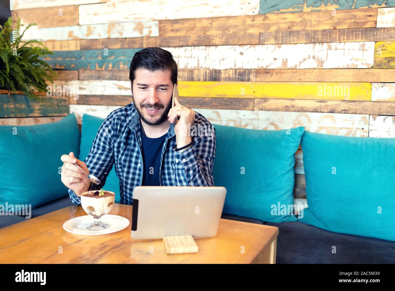 Remote working freelancer talking on phone in cafe while using digital tablet Stock Photo