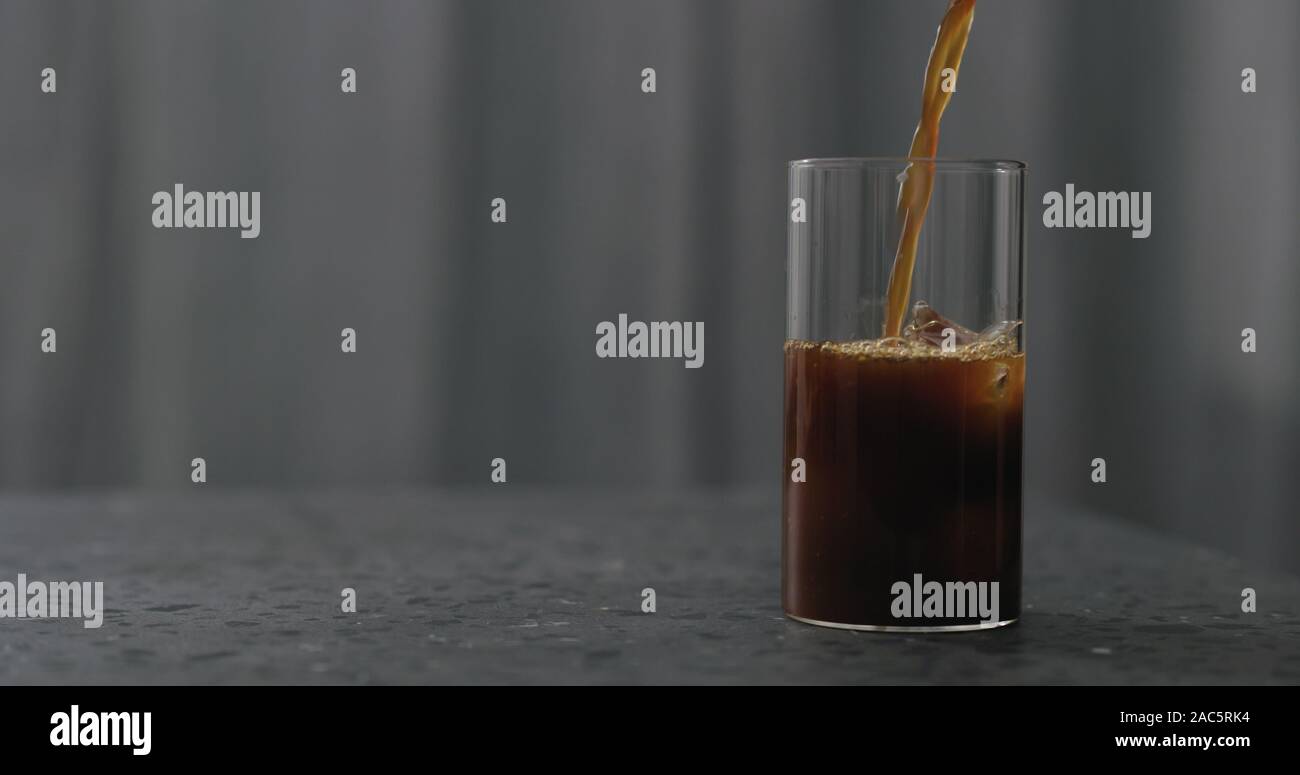 pour coffee over ice cubes in glass to make iced coffee on terrazzo