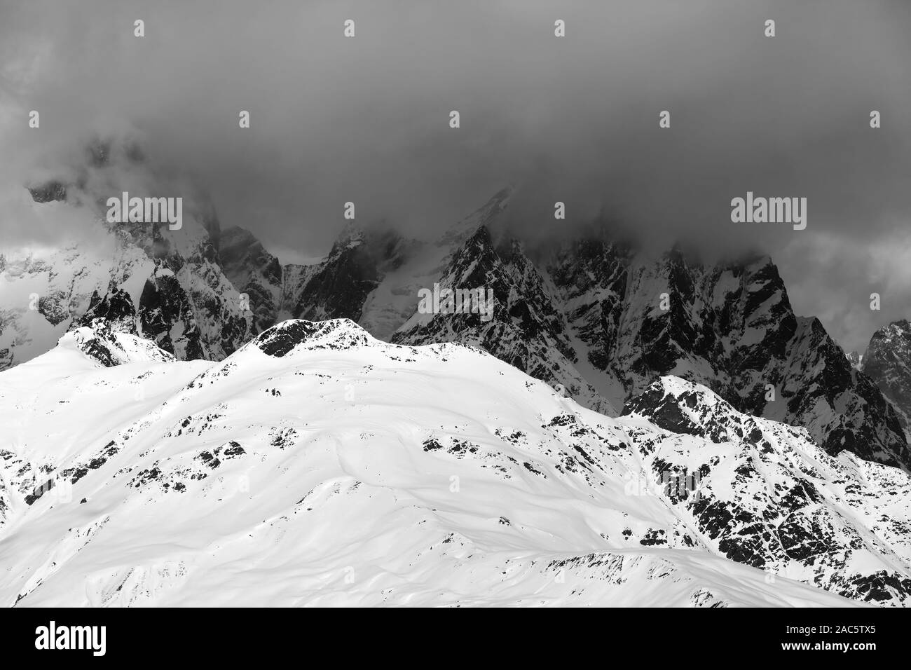 Snowy rocks in haze and storm clouds before blizzard at winter. Caucasus Mountains. Svaneti region of Georgia. Black and white toned landscape. Stock Photo
