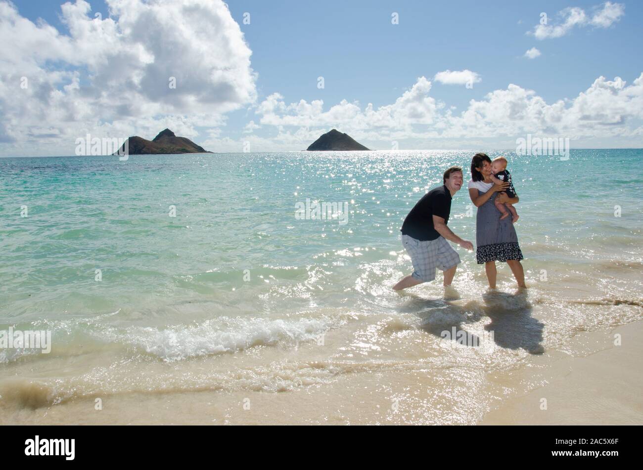 A family of three enjoying each other at Lanikai Beach, O'ahu, with the Mokulua Islands in the distance. Stock Photo