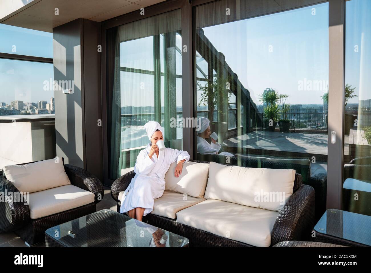 Young woman getting rest in bathrobe on terrace and drink coffee. Stock Photo