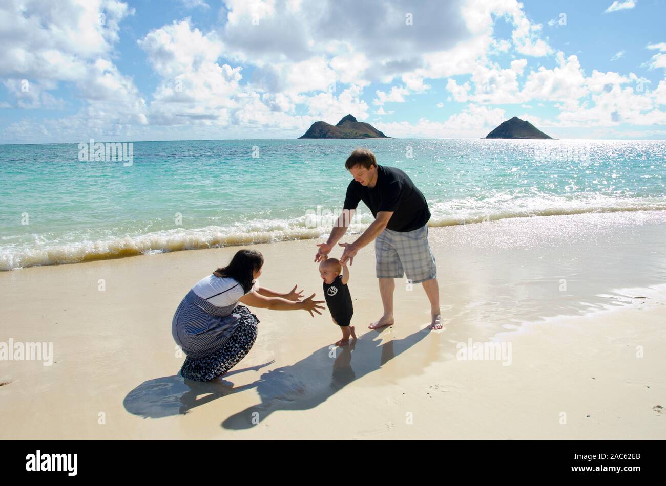 A family of three playing on Waimanalo Beach, O'ahu, with the Mokulua Islands in the distance. Stock Photo