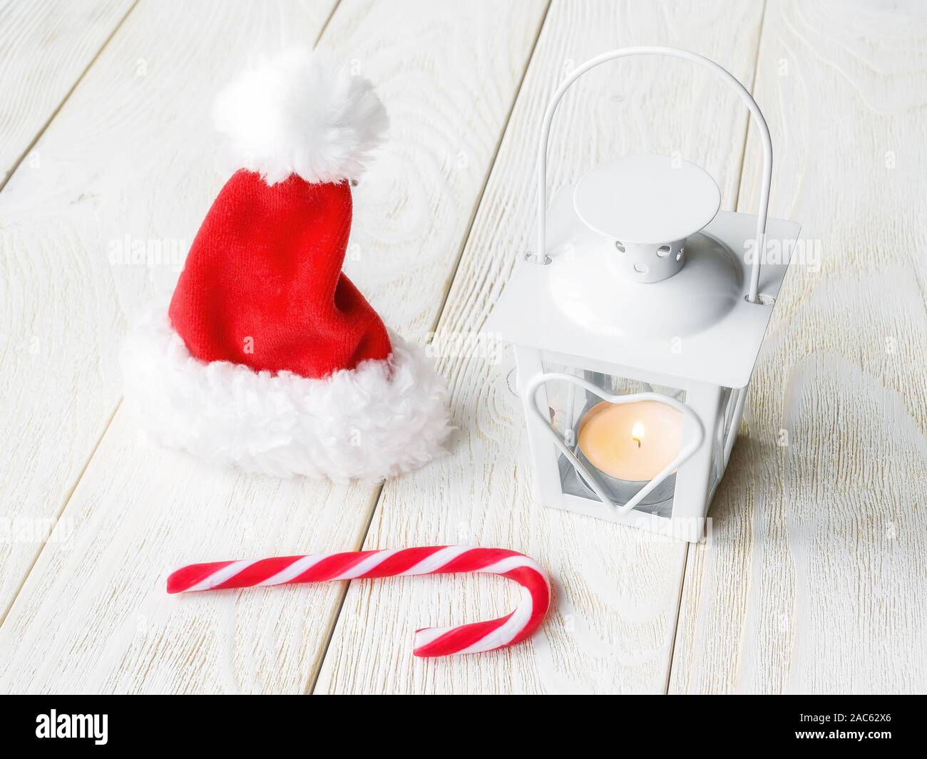 Santa Claus red hat, white lantern with a burning candle and sweet candy  cane on a white wooden surface. Christmas and New Year greeting card Stock  Photo - Alamy