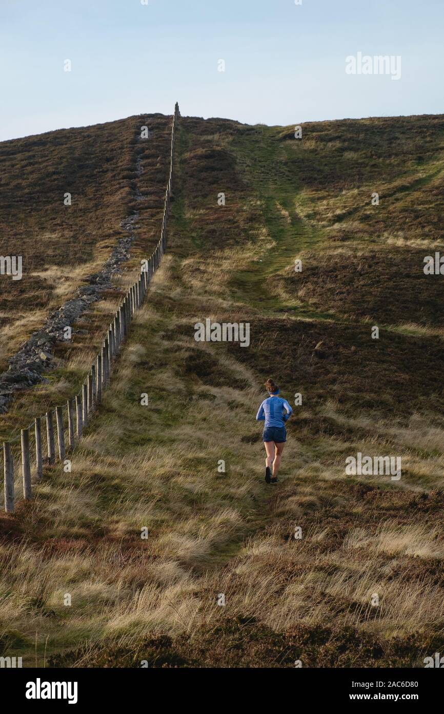 A woman is running among the Scottish hills in the park. The view from the back. Stock Photo