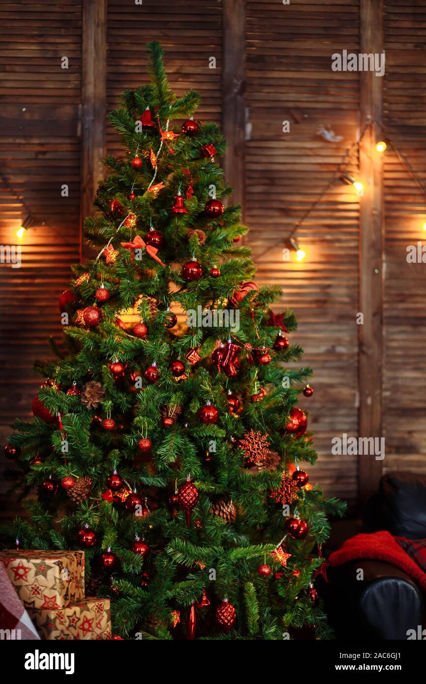 https://c8.alamy.com/comp/2AC6GJ1/green-christmas-tree-decorated-with-red-toys-ornaments-pine-cones-beads-garlands-box-sofa-wooden-wall-floor-2AC6GJ1.jpg