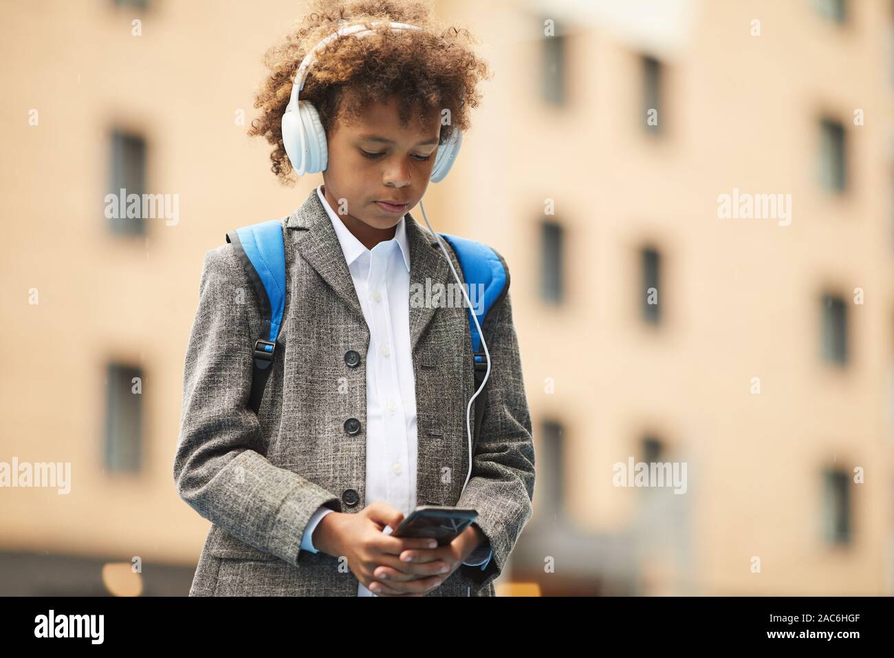 African schoolboy in headphones listening to music on his mobile phone while standing outdoors Stock Photo