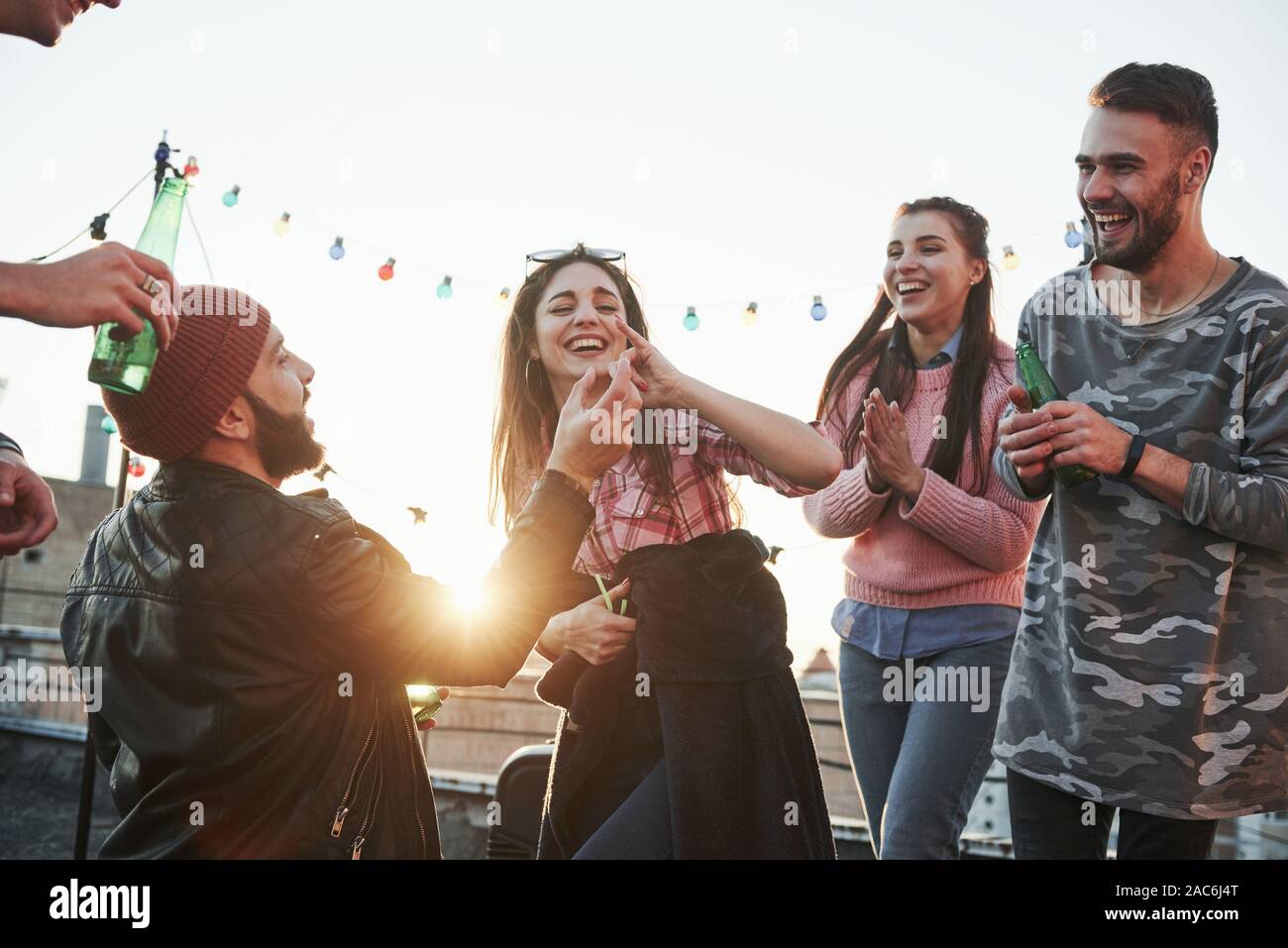 Wrong finger. Girl fooled the guy. Declaration of love on the rooftop with company of friends Stock Photo