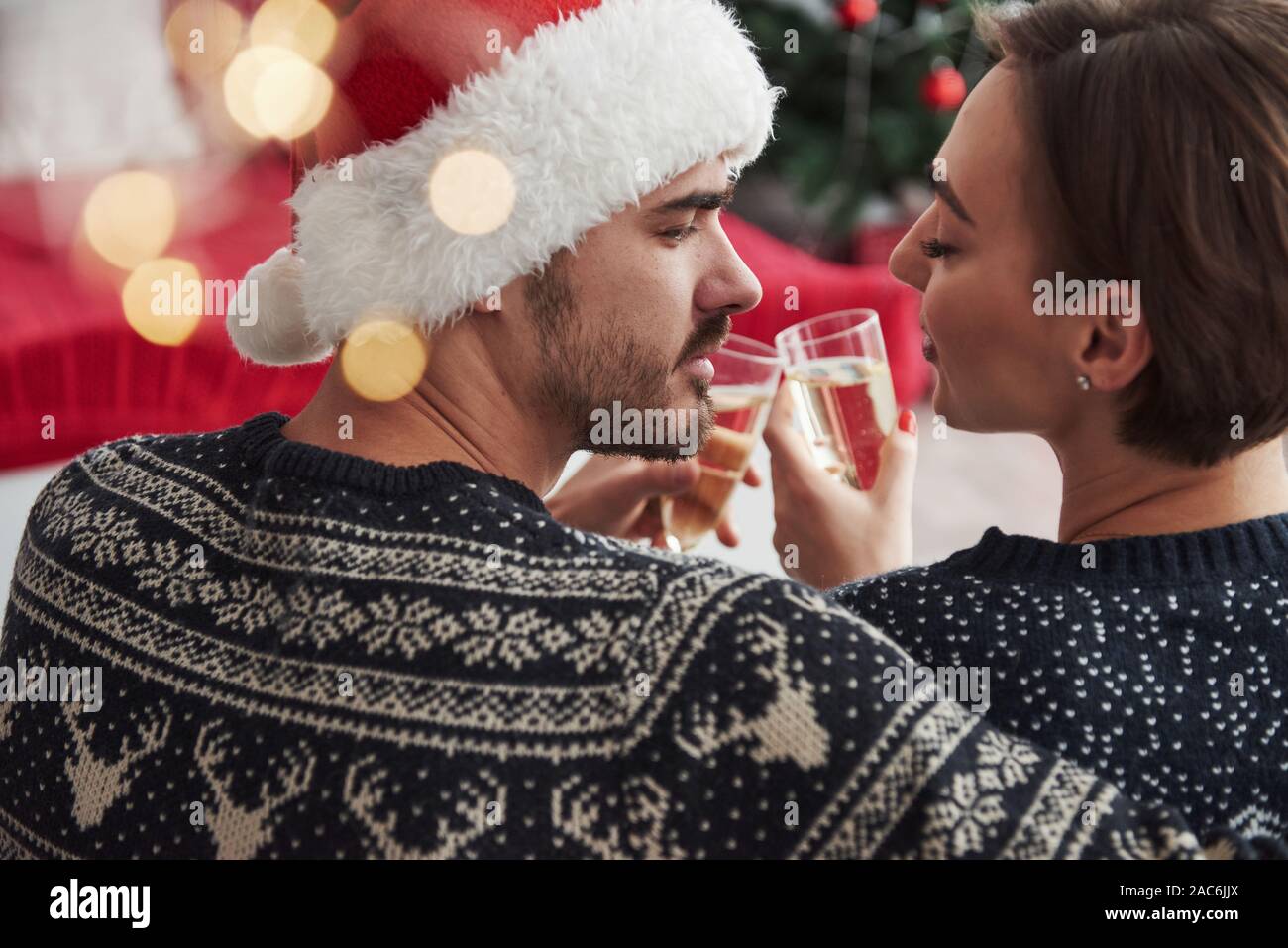 That's how love looking is. Celebrating new year. Knocking glasses. Beautiful couple in holiday clothes sits and hugs each other. Photo from the back Stock Photo