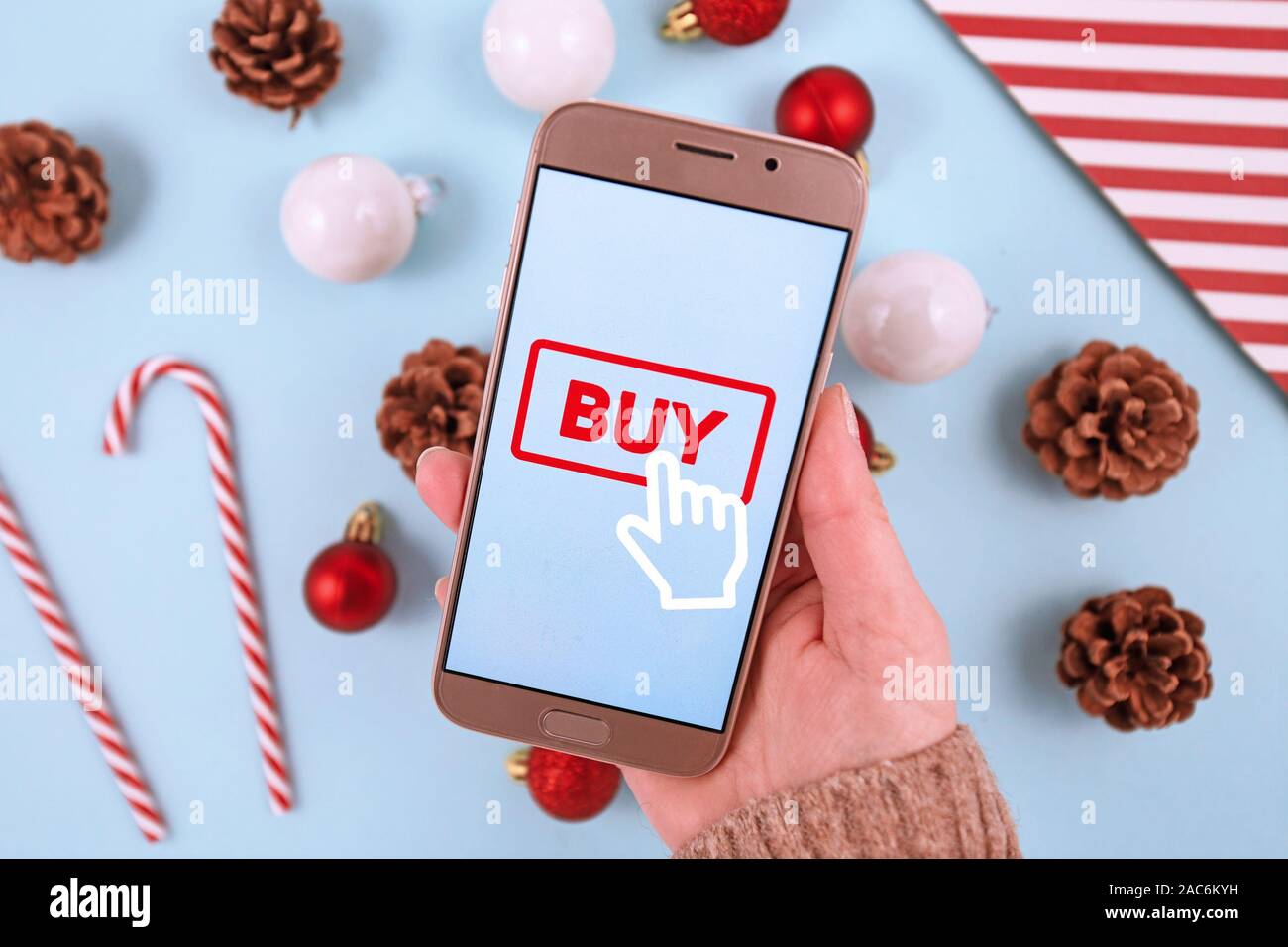 Concept for Christmas seasonal online shopping and sales with hand holding cell phone with 'Buy' click button sign in front of desk with seasonal deco Stock Photo