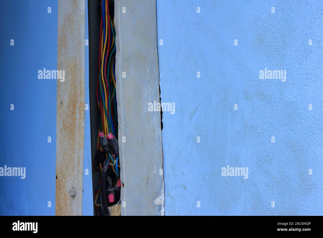 Closeup exposed power lines in broken wireway installed on dirty blue wall of a building Stock Photo