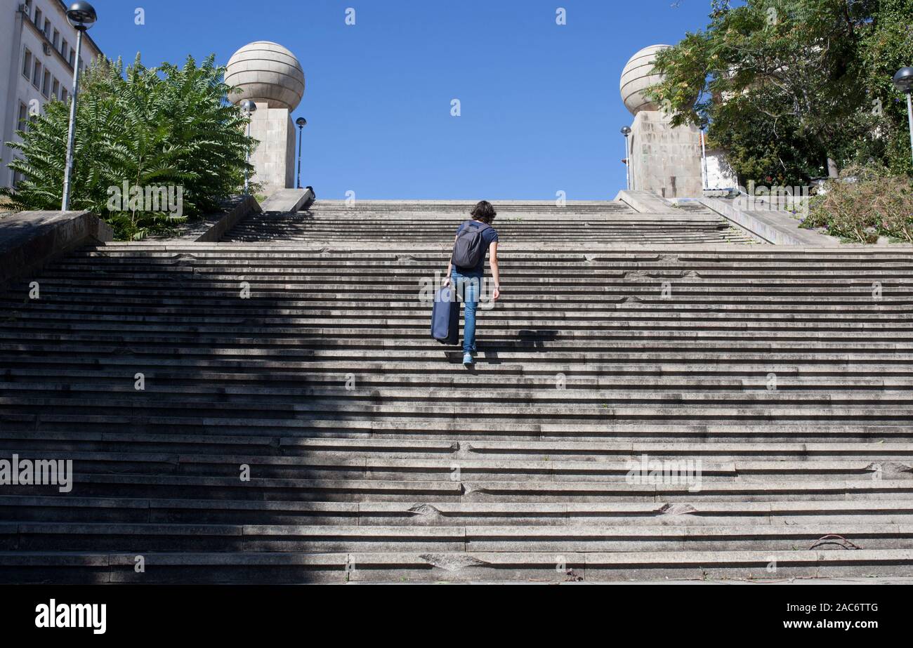 Young tourist woman going up the stairs with her heavy suitcase. Accessibility barriers of historic districts concept Stock Photo