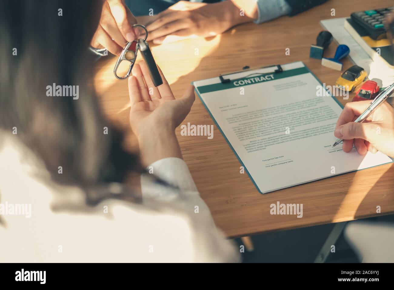 dealer salesman giving car key to new owner. client signing ...