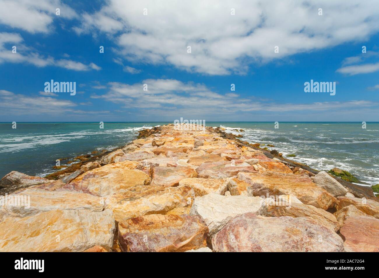 Rocks breakwater and white clouds in blue sky Stock Photo - Alamy