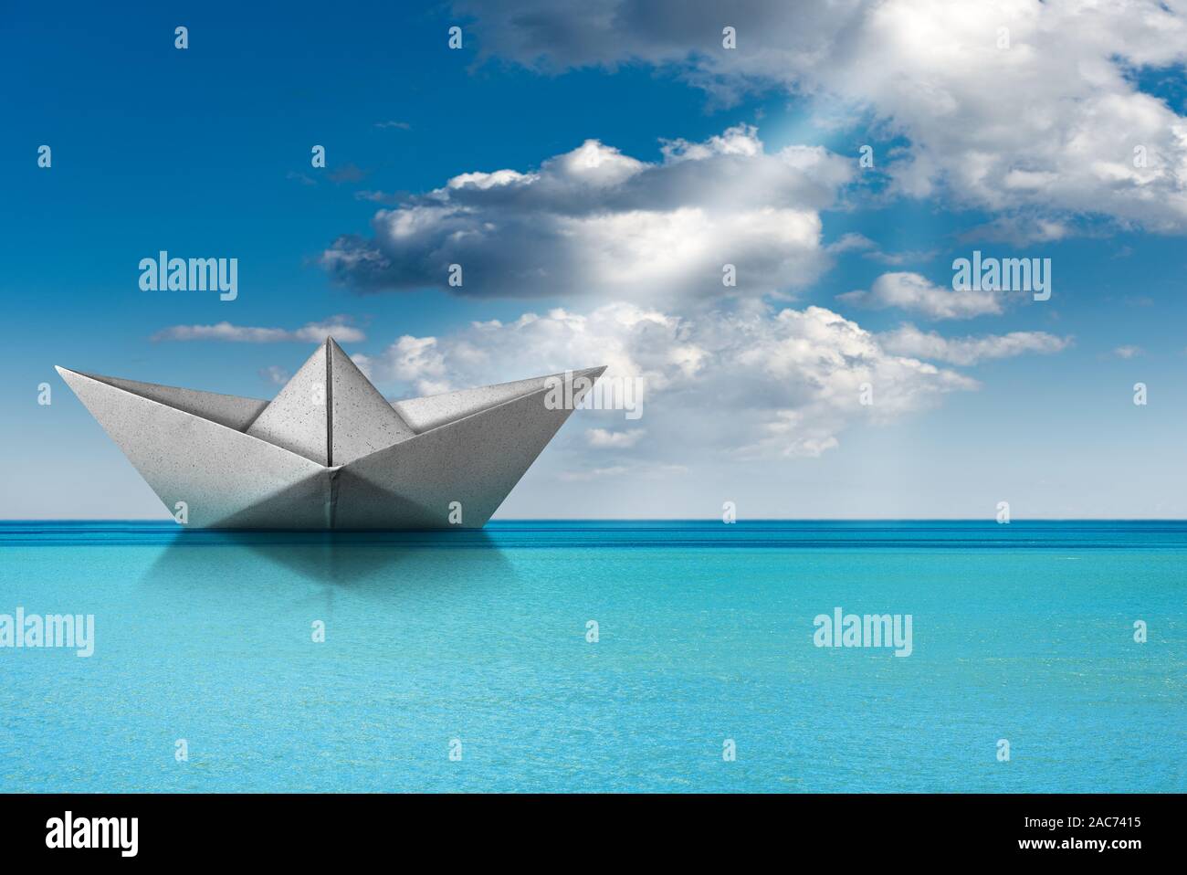 White paper boat, origami, in the turquoise sea with blue sky, clouds and sun rays Stock Photo