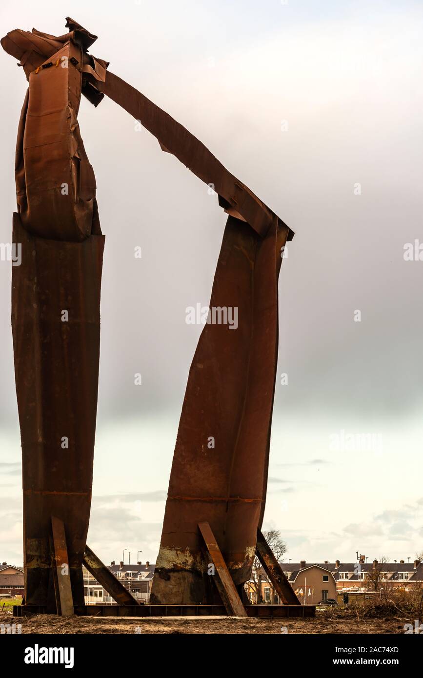tall rusty colored artwork made out of of steel standing near a residential area Stock Photo