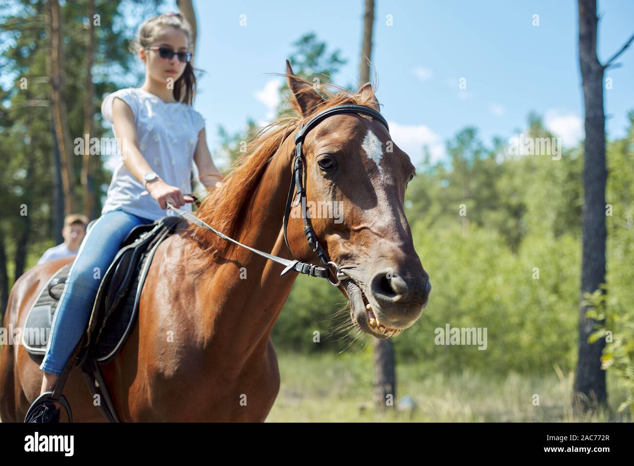 Close up of brown horse running with teenage rider girl, horse face looking at the camera Stock Photo