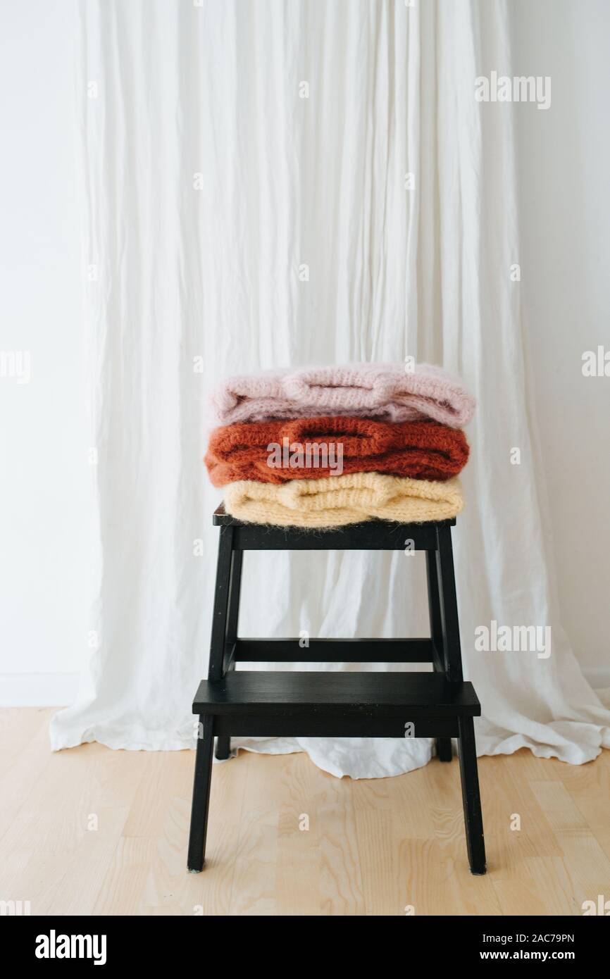 Three folded multi-colored sweaters lie on stepping stool in front of a curtain Stock Photo