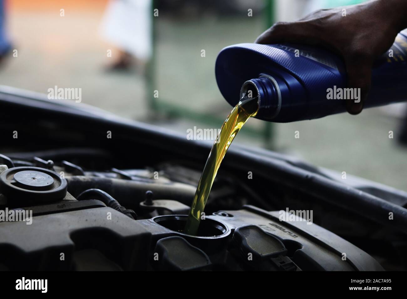 Mechanic pours motor oil into engine from blue plastic container Stock Photo