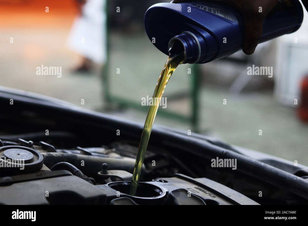 Mechanic pours motor oil into engine from blue plastic container hires