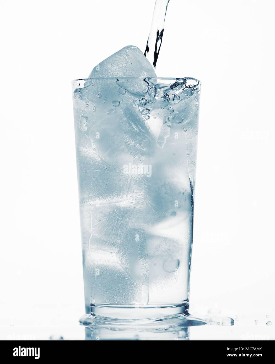 pouring water in a glass full of ice cubes, white background, blue ...