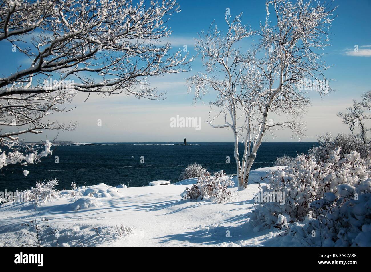 The snow covered rocky coastline at Fort Williams Park and ram island ledge light station in portland Maine on a sunny blue sky day. Stock Photo