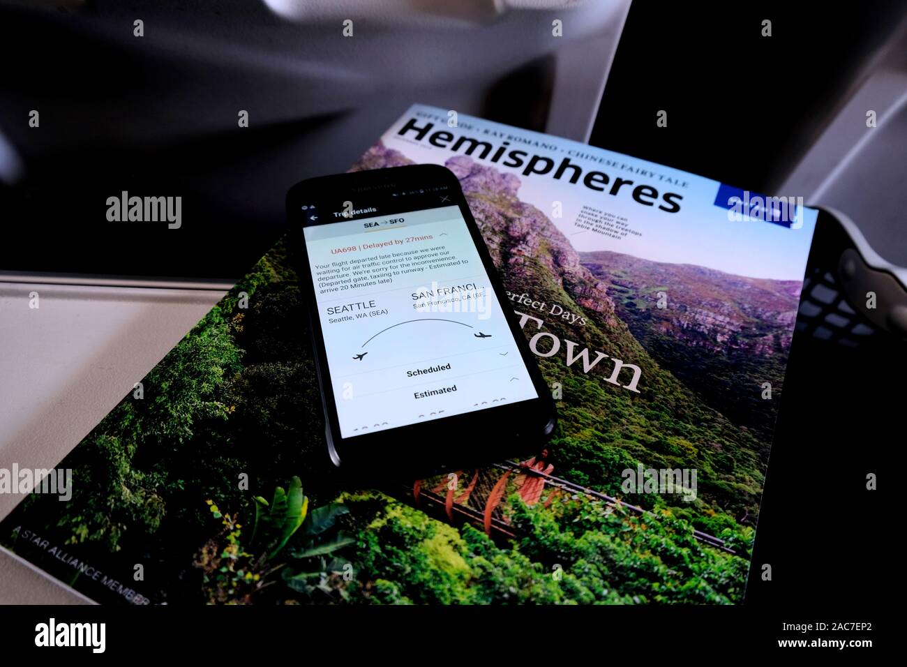 United Airlines Hemispheres Magazine on a tray table with a cell phone screen showing a delayed flight departure from Seattle to San Francisco. Stock Photo
