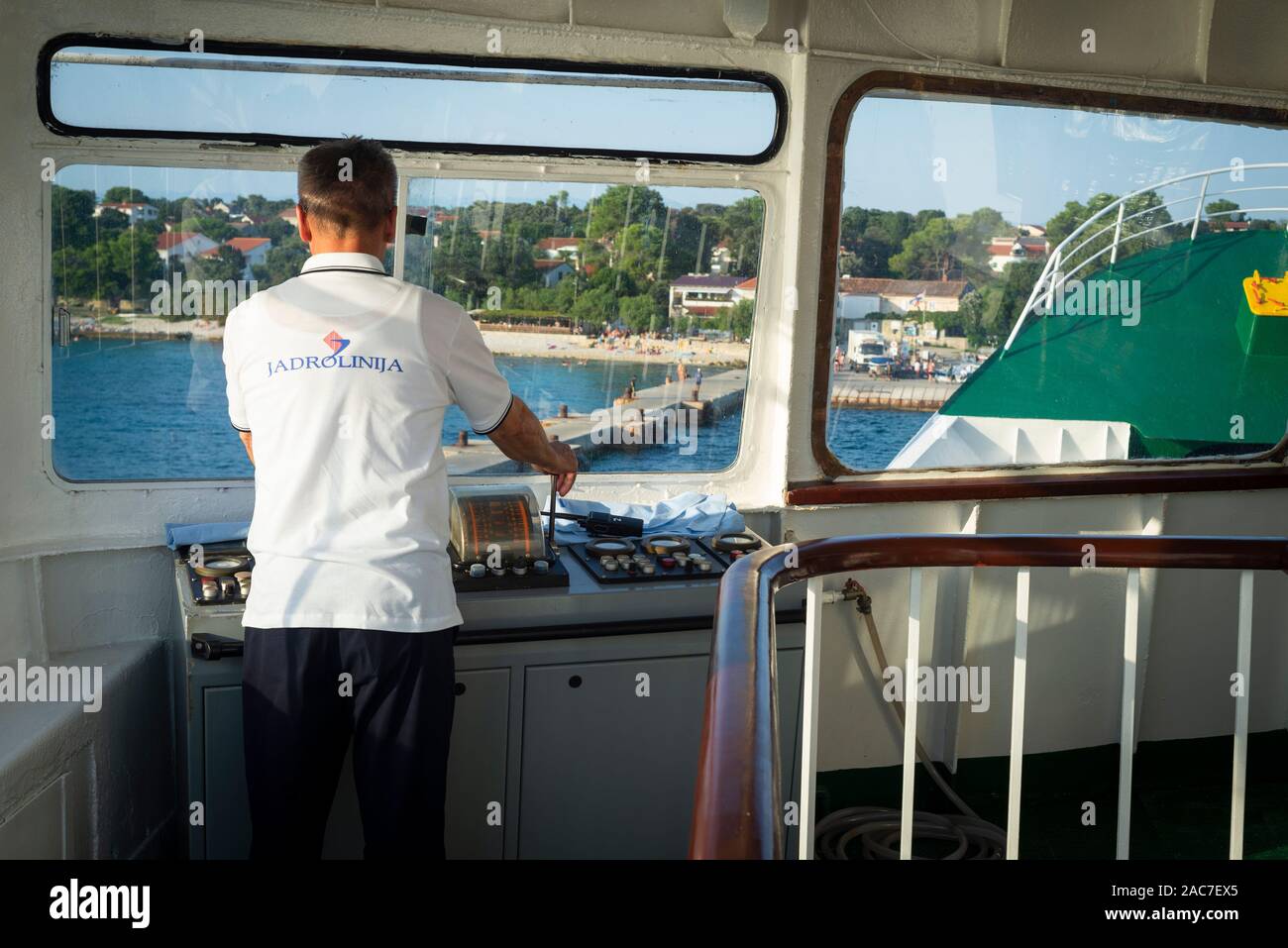 The helmsman of a car ferry stands on the bridge and directs the ship to the pier in the harbor on the island of Silba, Kvarner Bay, Croatia Stock Photo