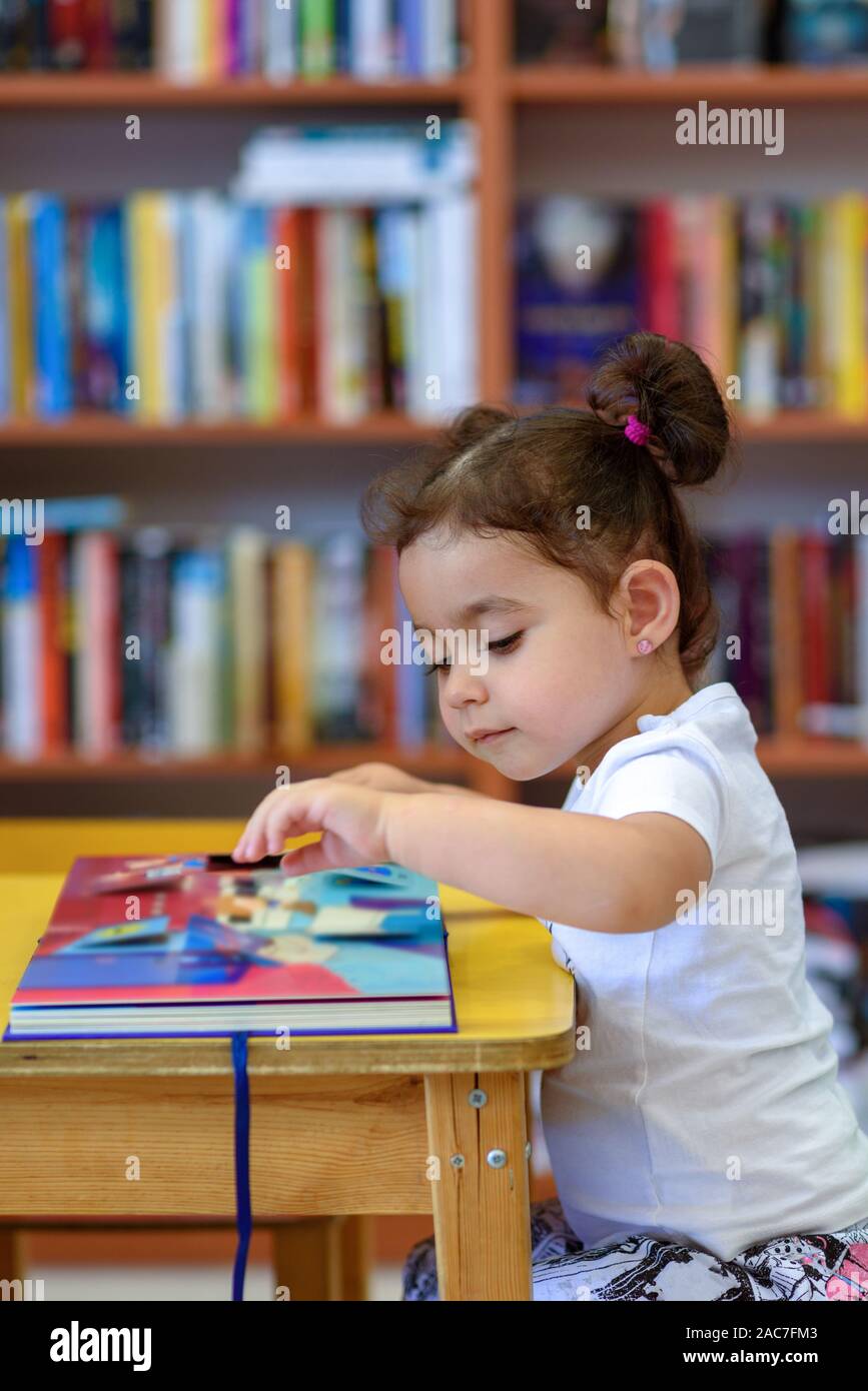 Little Girl Indoors In Front Of Books. Cute Young Toddler Sitting On A