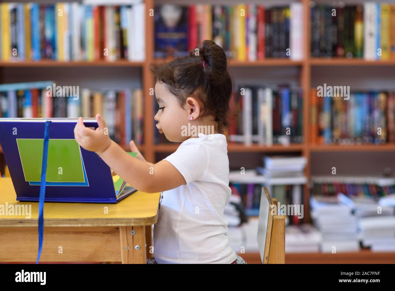 Little Girl Indoors In Front Of Books. Cute Young Toddler Sitting On A