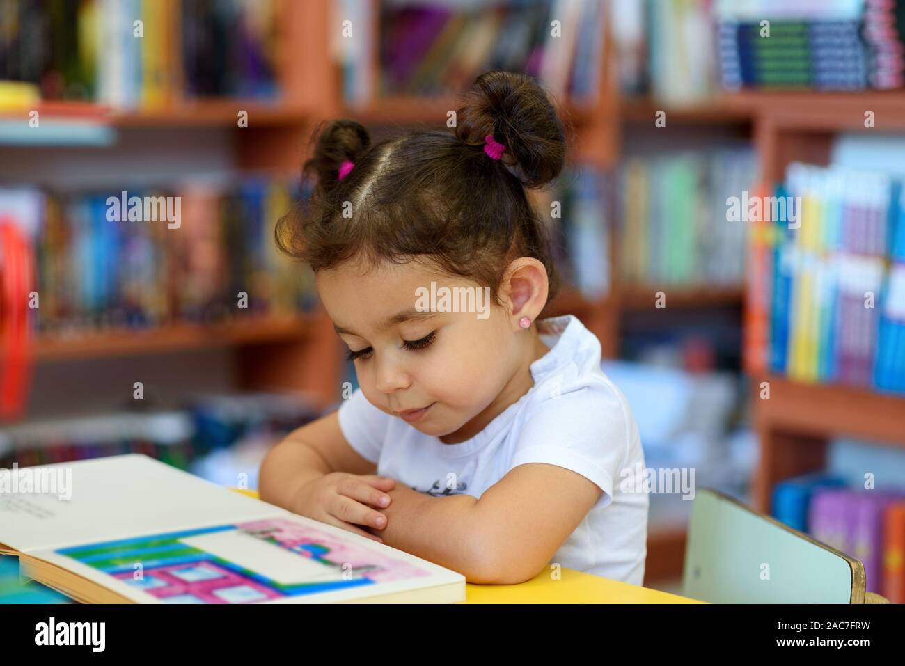 Little Girl Indoors In Front Of Books. Cute Young Toddler Sitting On A
