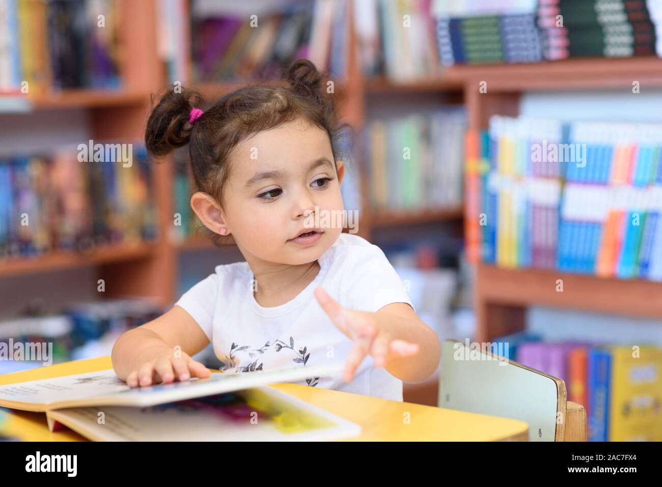 Little Girl Indoors In Front Of Books. Cute Young Toddler Sitting On A
