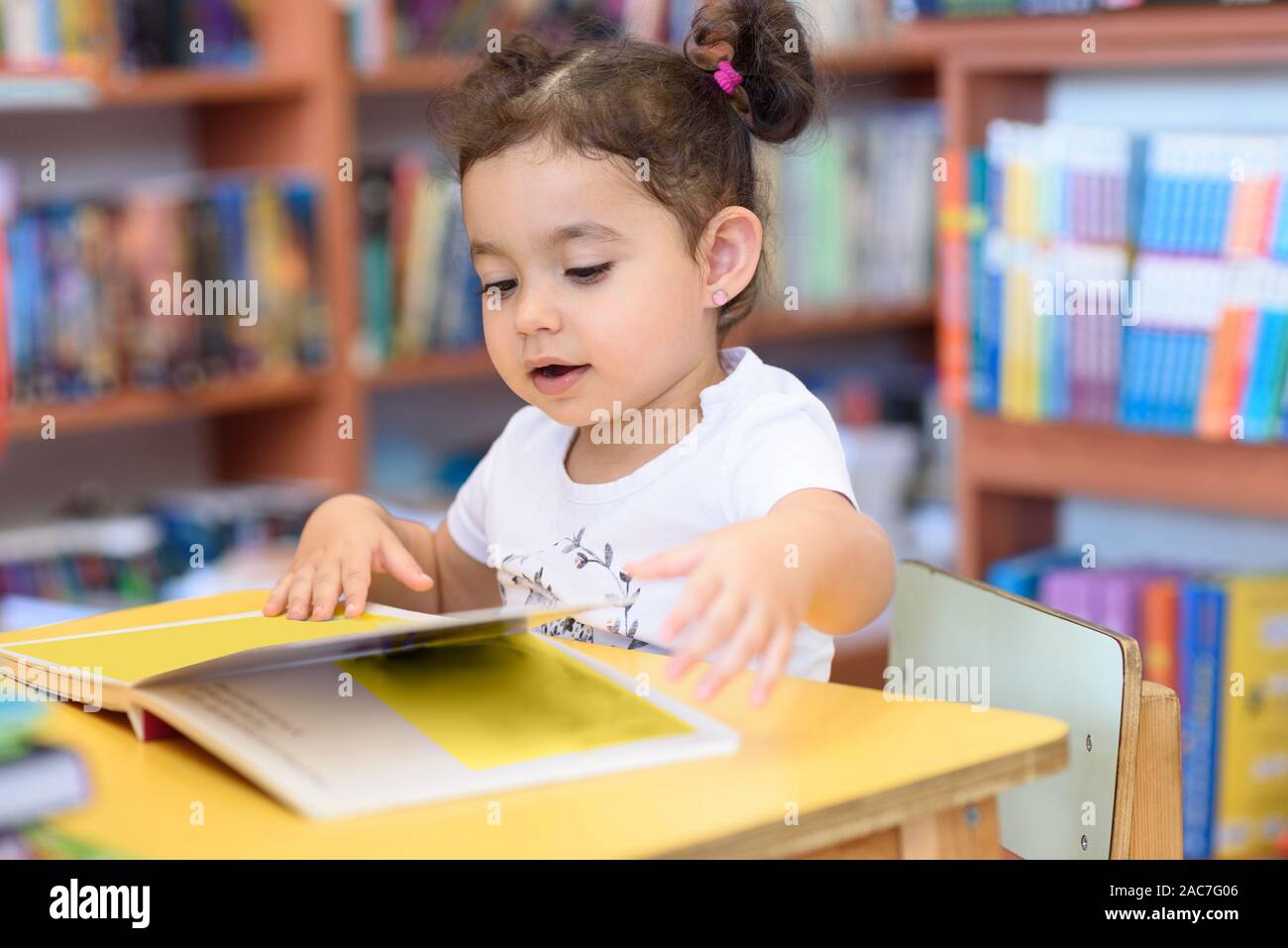 Little Girl Indoors In Front Of Books. Cute Young Toddler Sitting On A