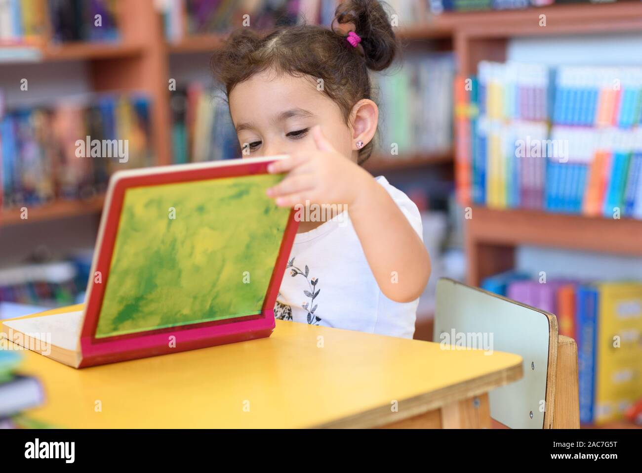 Little Girl Indoors In Front Of Books. Cute Young Toddler Sitting On A