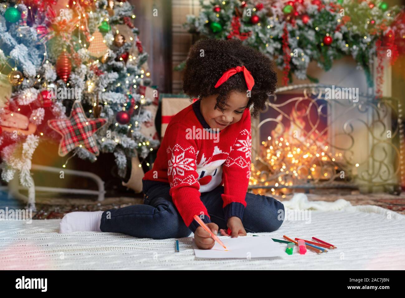 Sweet little girl writing letter to Santa in decorated living room Stock Photo