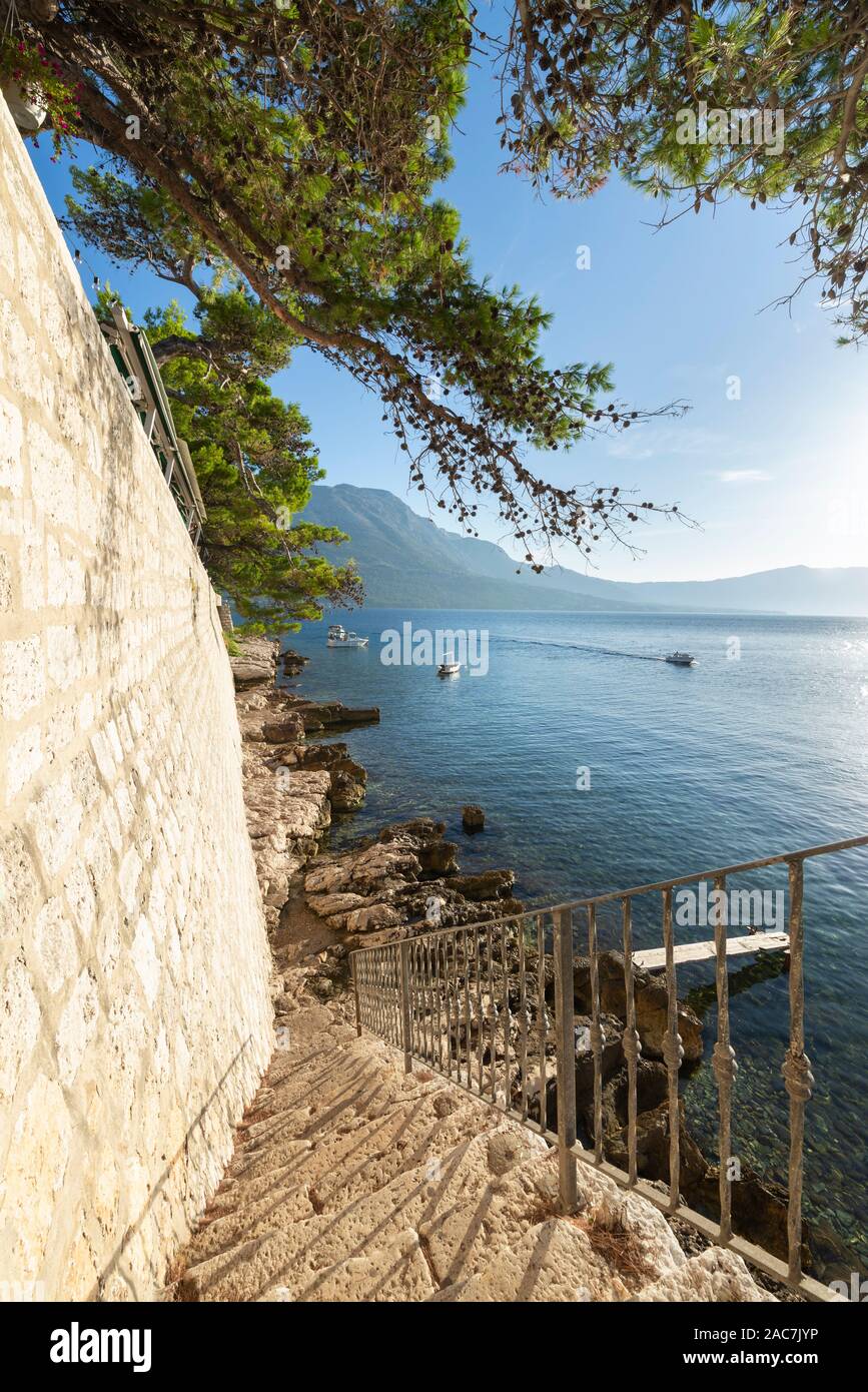 Stairs down to rocks on the water below the city wall of Korcula with a view of the sea and mountains of Peljesac, Dalmatia, Croatia Stock Photo
