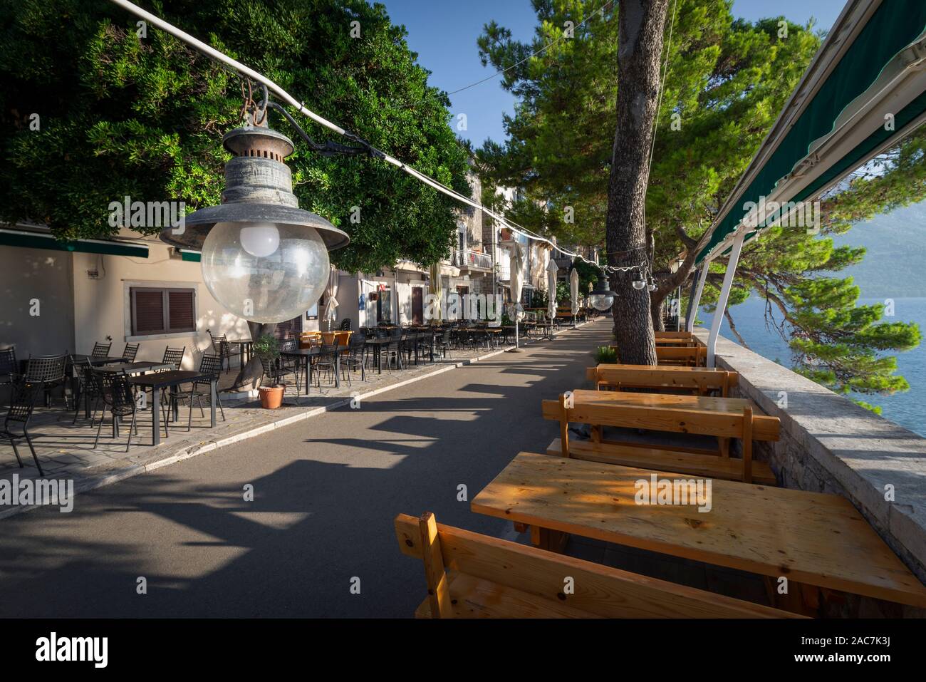 Lamp in front of empty tables and chairs on the terrace of the restaurants on the town wall of the old town of Korčula in the morning sun, Croatia Stock Photo