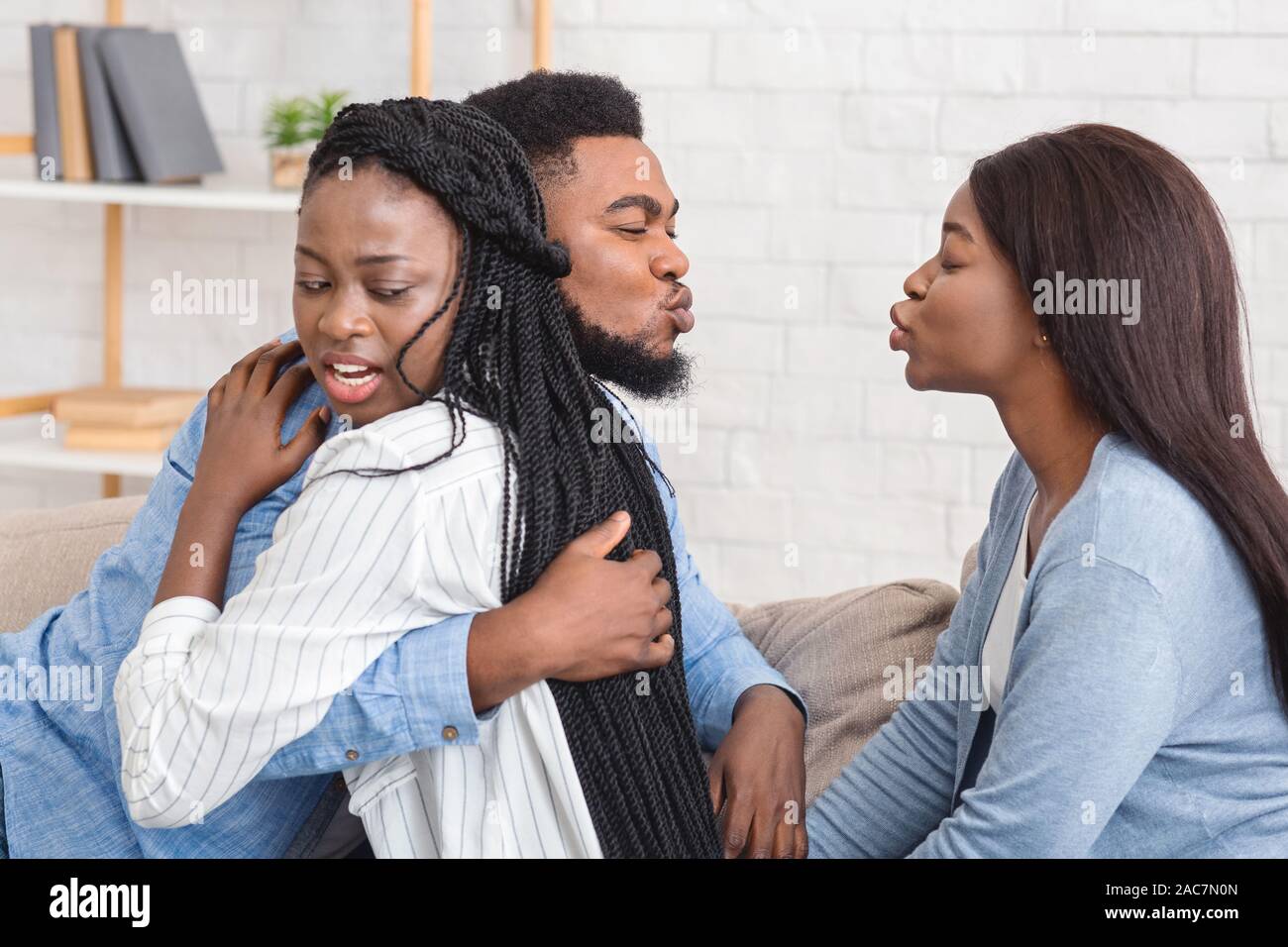 Unfaithful Black Boyfriend Kissing Another Girl While Hugging His Girlfriend Stock Photo
